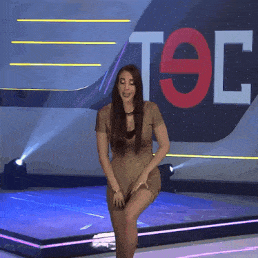 a woman stands on a stage in front of a sign that says t9c