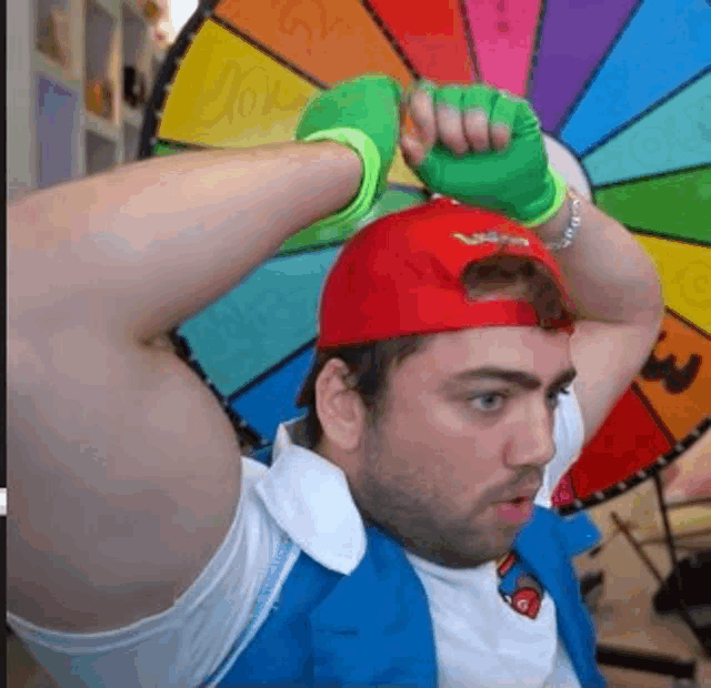 a man wearing a red hat and green gloves is standing in front of a colorful wheel