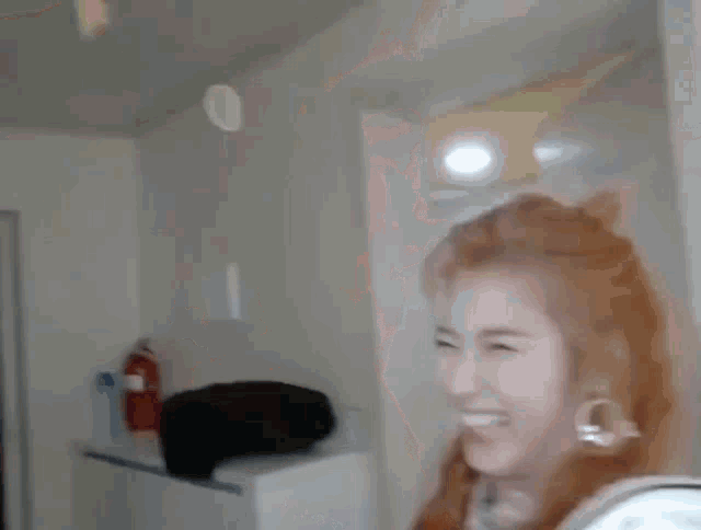 a woman with red hair is laughing in a room with a fire extinguisher in the background .