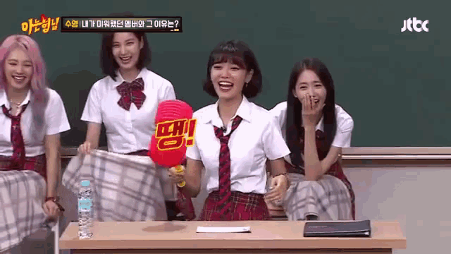 a group of girls in school uniforms are sitting at a table with a fan that says ' tbc ' on it