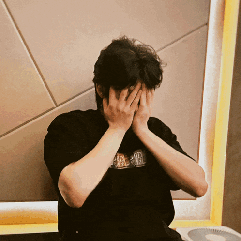 a man covering his face with his hands wearing a black t-shirt that says dd