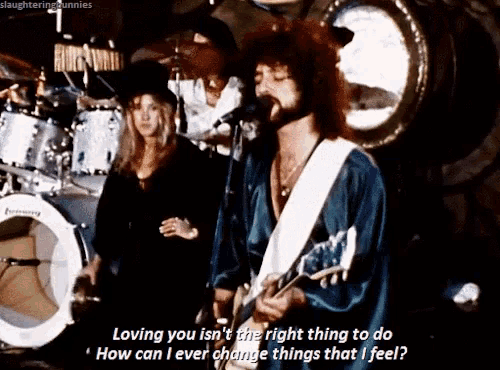 a man singing into a microphone while playing a guitar and a woman stands behind him