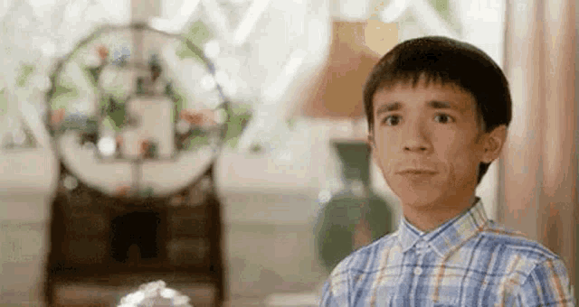 a young boy in a plaid shirt is making a funny face while sitting in a living room .