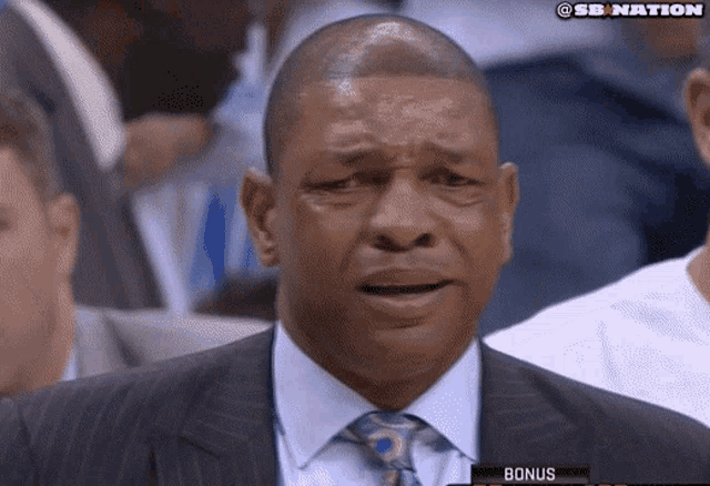 a man in a suit and tie is sitting in a stadium with a sign that says bonus