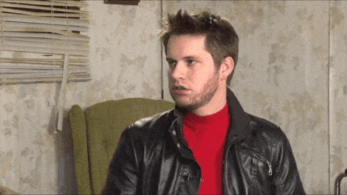 a man with a beard wearing a leather jacket and a red turtleneck