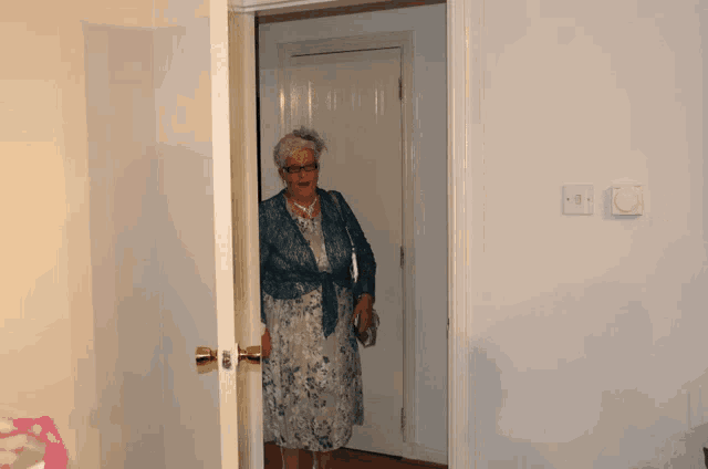an elderly woman in a blue dress is standing in a doorway
