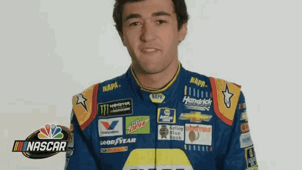 a man wearing a blue and yellow nascar jacket is making a funny face .