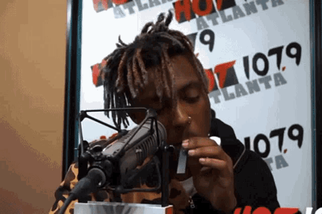 a man is smoking a cigarette in front of a microphone in front of a sign that says 1079 atlanta