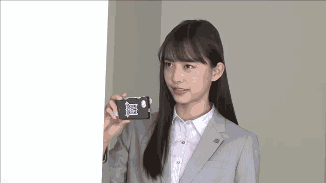 a girl in a suit is holding a cell phone with a sticker on it