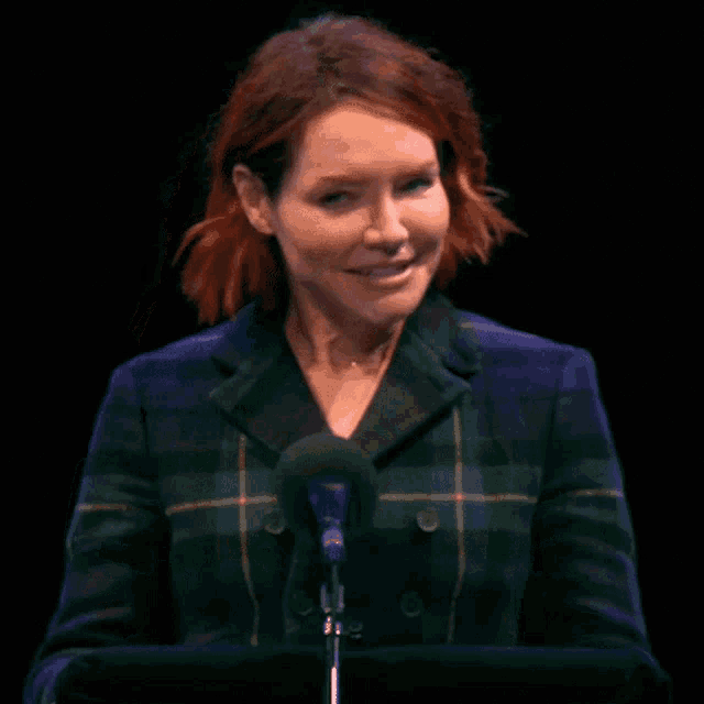 a woman in a plaid jacket is smiling while speaking into a microphone