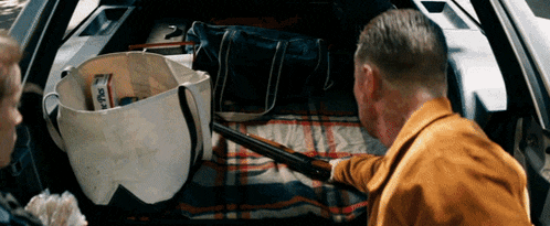 a man is holding a shotgun in the back of a car while another man looks on