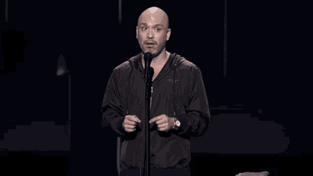 a bald man in a black jacket is standing in front of a microphone and says uh-oh .