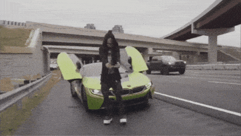 a man in a hooded jacket stands next to a green sports car