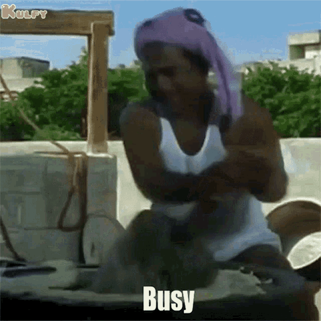 a man wearing a purple head scarf is sitting on a table with the word busy written on the bottom .