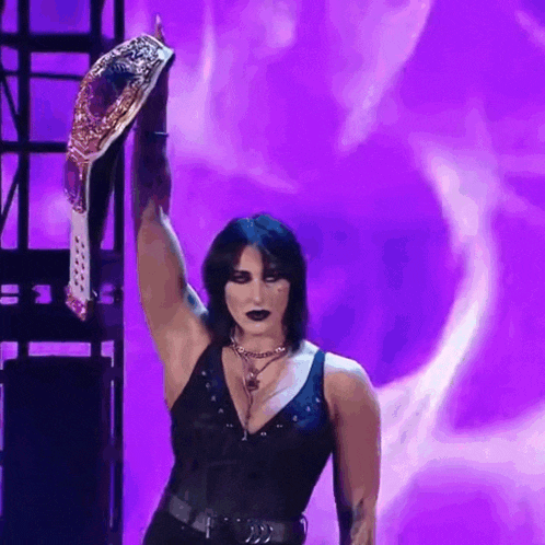 a woman in a black tank top is holding a wrestling championship belt in front of a purple background