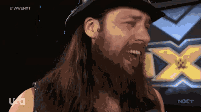 a man with long hair and a hat is smiling in front of a wwe logo