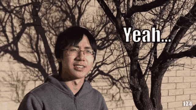 a man wearing glasses is standing in front of a tree and says yeah