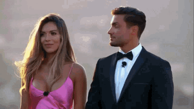 a man in a suit and a woman in a pink dress are holding hands .