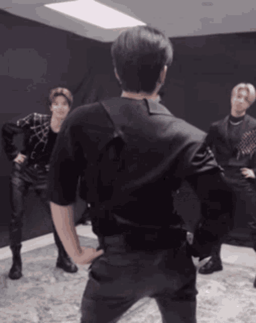 a man in a black shirt is standing with his hands on his hips in a room with other men .