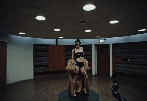 a woman in a fur coat stands in a dark room with an exit sign