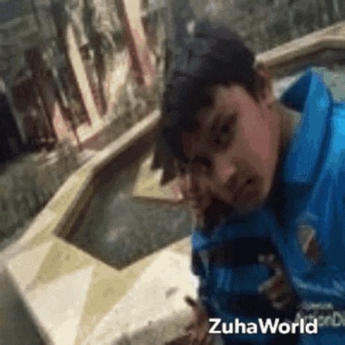 a young boy in a blue shirt is standing in front of a fountain with the words zuhaworld on the bottom
