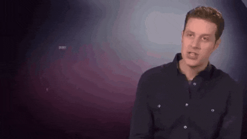 a man in a black shirt is making a funny face while standing in front of a purple background .