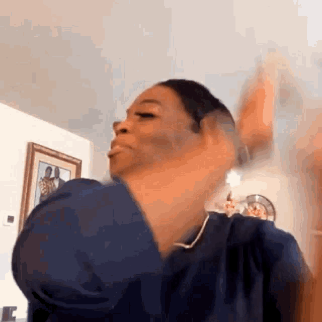 a woman in a blue shirt is making a funny face while standing in a living room .