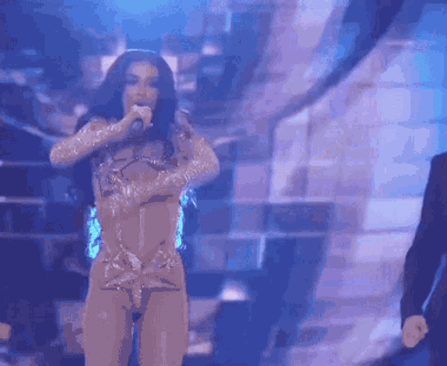 a woman is singing into a microphone on a stage while a man stands behind her .