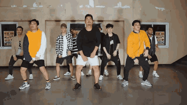 a group of young men are dancing in a room with a sign on the wall that says ' kick ass '