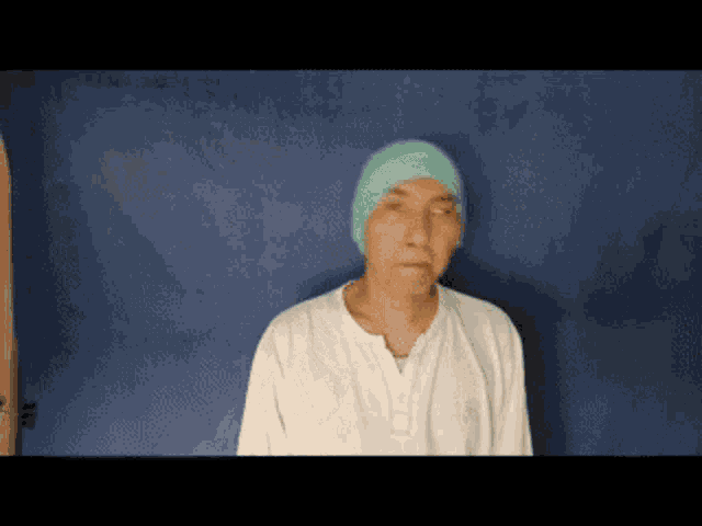 a man wearing a white shirt and a green hat is standing in front of a blue background