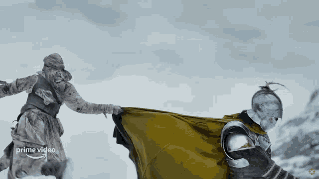 a man in a knight 's armor is holding another man 's hand in the snow