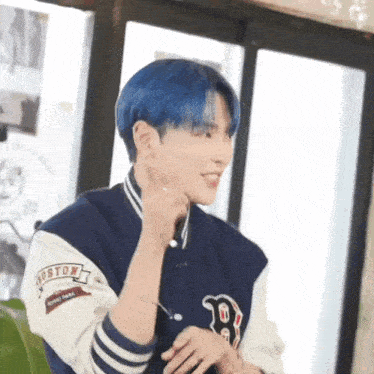 a man with blue hair is wearing a boston baseball jacket and earrings .