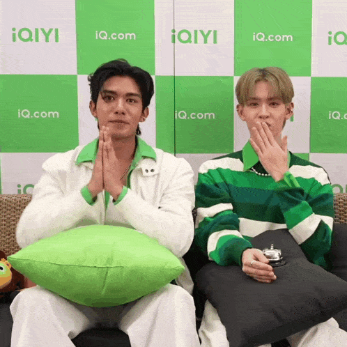 two men are sitting on a couch in front of a wall with iq.com written on it