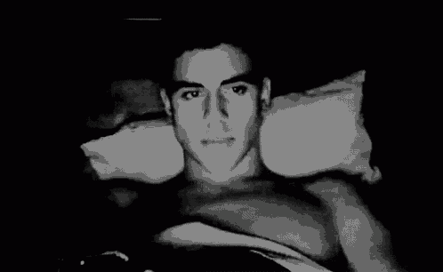 a black and white photo of a shirtless man laying on a bed