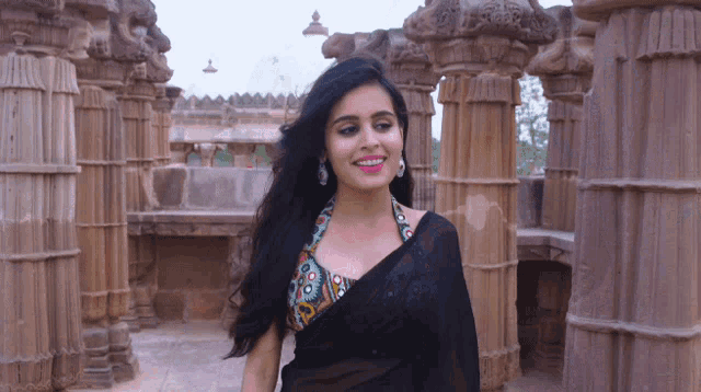 a woman in a black saree smiles in front of a row of pillars