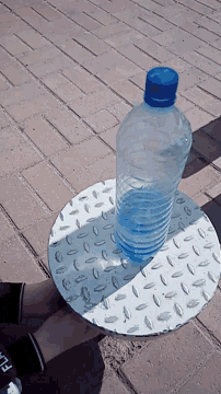 a bottle of water sits on top of a metal plate with a brick background