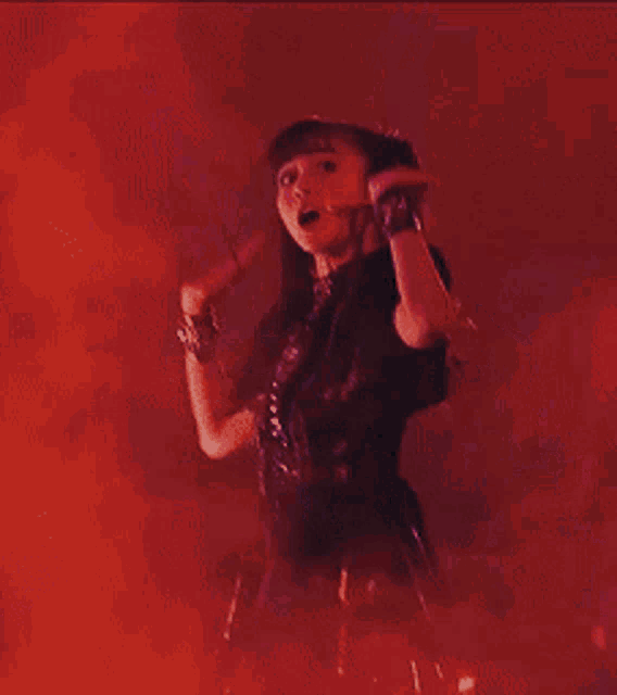 a woman in a black dress is dancing in a dark room with her arms in the air