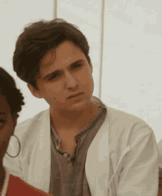 a young man wearing a white coat looks at the camera