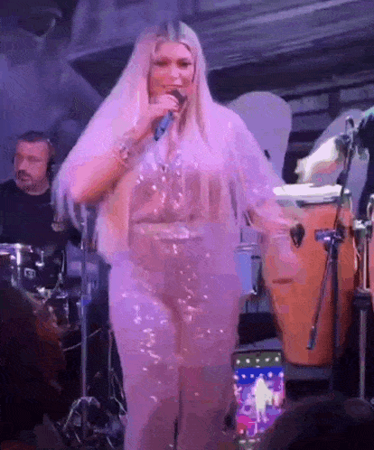 a woman with long blonde hair is singing into a microphone on stage .