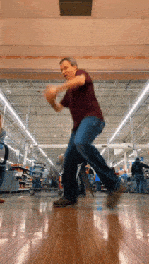 a man in a maroon shirt is dancing in a grocery store