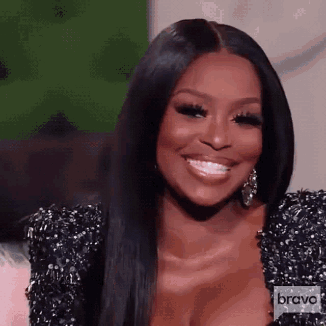 a woman wearing a black dress and earrings is smiling while sitting on a couch .