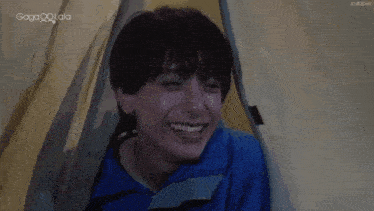 a young man in a blue shirt is smiling while sitting in a tent .