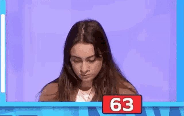 a woman is sitting in front of a blue screen with a red sign that says 63 .