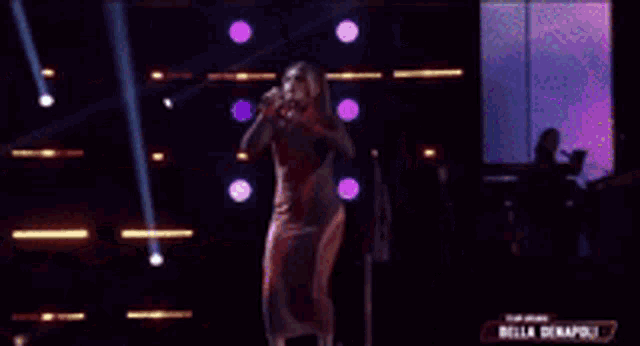 a woman in a red dress is singing into a microphone in front of a wall of lights