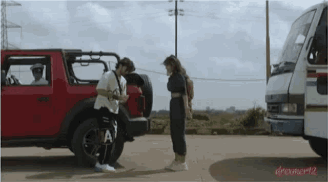 a man and a woman are standing next to each other in front of a red jeep .