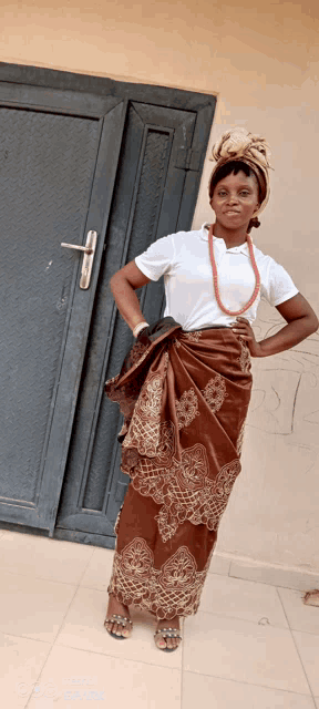a woman standing in front of a door wearing a white shirt and a brown skirt