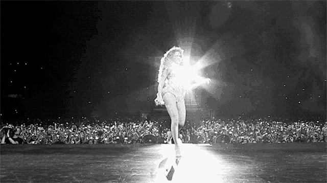 a black and white photo of a woman dancing on a stage in front of a crowd of people .