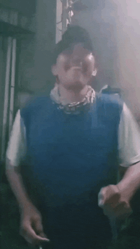 a man in a blue vest is smoking a cigarette while wearing a hat .