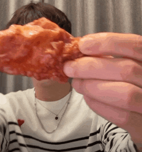 a man wearing a striped shirt is holding a piece of fried chicken in front of his face