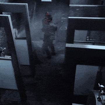 a man in a red jacket is standing in a dark room with water spraying out of a window